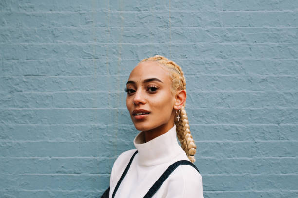 Portrait of a fashionable, young woman in Lower Manhattan, New York Vintage toned portrait of a young mixed race Latina woman from New York. She is sporting striking blond braids, leaning against the pastel toned brick wall. gen z stock pictures, royalty-free photos & images