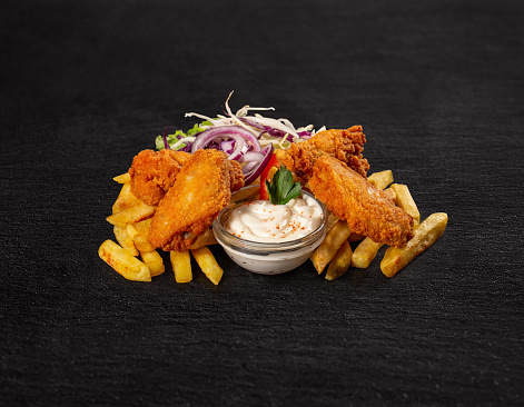 Crispy chicken wings with french fries on black slate background
