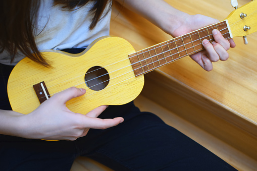 Girl hands playing song on small yellow ukulele guitar. Music and hobbies concept.