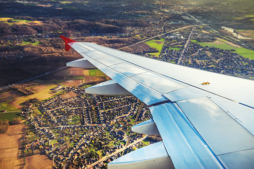 Wing of an airplane flying above the city land.