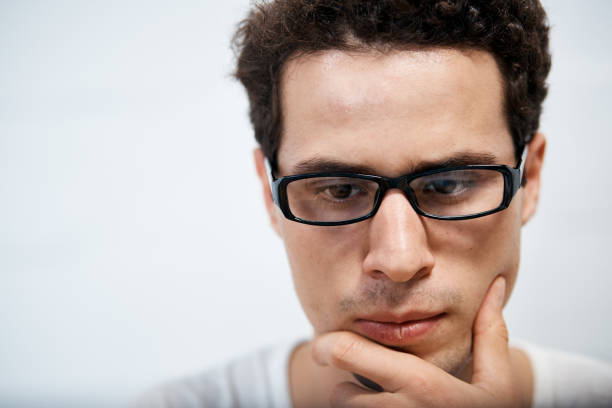 A handsome young man looks down, serious and thinking, his hand on his chin.