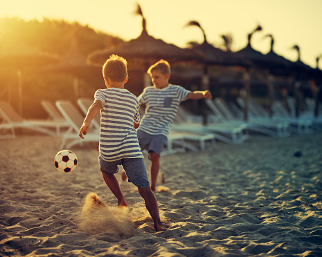 Little boys aged 9 playing soccer on beach. Summer vacations day sunset.\nNikon D810