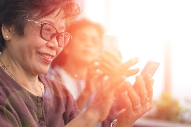 fröhliche senioren senioren gesellschaft lifestyle konzept. älte asien-frauen, die smartphones nutzen, teilen sich soziale medien in der wohlfühlregion zu hause zusammen. - 40 weeks stock-fotos und bilder
