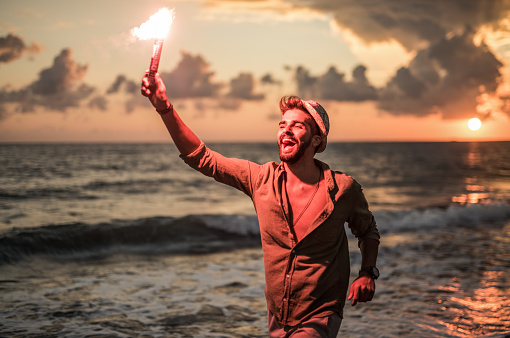 Ecstatic young man running with a torch on the beach.