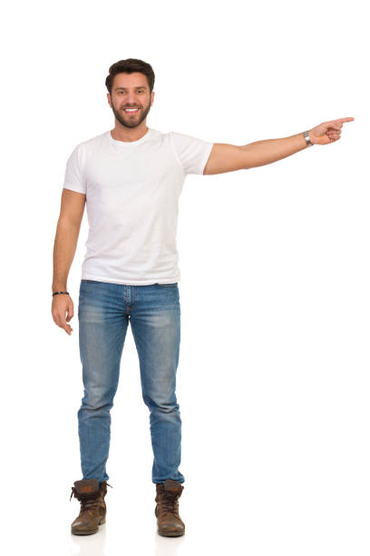 istock Young Man In Jeans And White T-shirt Is Standing, Smiling And Pointing. Front View 1140078269