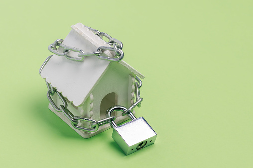 Toy house wrapped with a chain with a large lock on a green background as a symbol of the sanctity of the home
