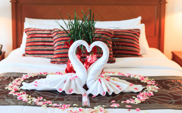 ロマンチックな寝室のインテリア、キス白鳥折り紙タオルと新婚カップルのためのベッドの上に花の花びらの装飾を振りかけ新鮮なピンクの白いバラ。結婚式、記念日、新婚旅行、愛、シン� - honeymoon romance wedding bedroom ストックフォトと画像