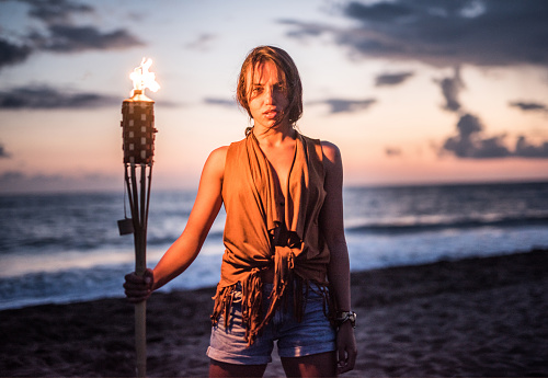 Young wild woman holding a torch on the beach.