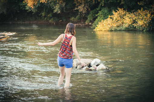 A caucasian girl in summer shorts crossing the river