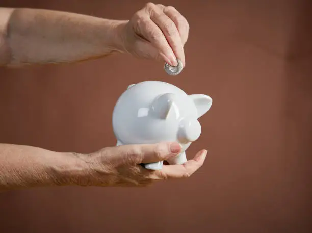 Photo of Senior person's hand adds coin to piggybank