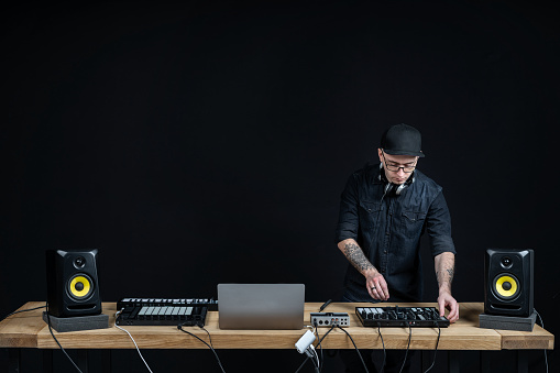 Adult and concentrated DJ master. Man using controller and records music inside house room studio with black dark wall interior and copy empty space for text