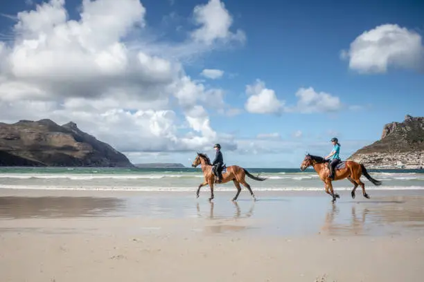 Photo of Two teenage girls riding horses on the beach