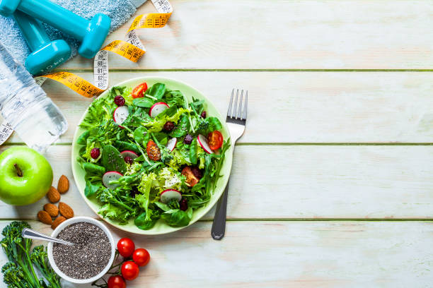 gesundes essen und bewegung im hintergrund: frischer gesunder salat, hanteln und tonbandmaß mit kopierplatz - superfood food healthy eating healthy lifestyle stock-fotos und bilder