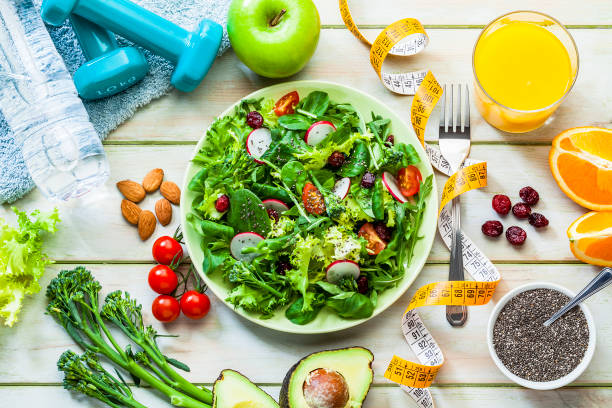 健康的な食事と運動の概念: フレッシュヘルシーサラダ、ダンベルと巻尺 - nut directly above multi colored food ストックフォトと画像