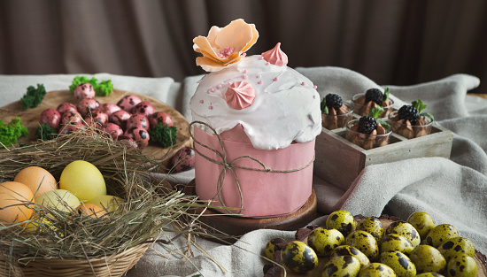 Traditional Easter sweet cake decorated with pink meringue and various coloured eggs on light background