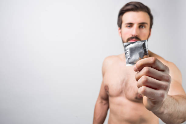 homem farpado considerável sem uma camisa, mostrando um preservativo. é bom usá-lo para evitar coisas ruins inesperadas com as pessoas. anunciando o conceito. contracepção. isolado no fundo branco - control clothing outdoors image technique - fotografias e filmes do acervo