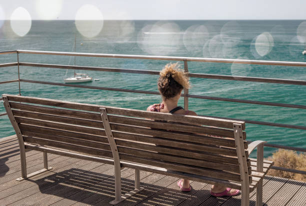istock woman sitting on a bench facing the ocean 1140115742