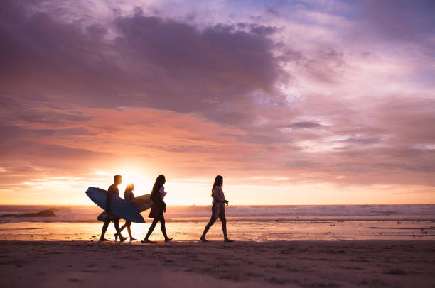 amis marchant sur la plage le soir - horizontal men women surfboard photos et images de collection