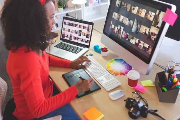 Female graphic designer using graphic tablet at desk Side view of young mixed-race female graphic designer using graphic tablet at desk in a modern office graphic designer stock pictures, royalty-free photos & images