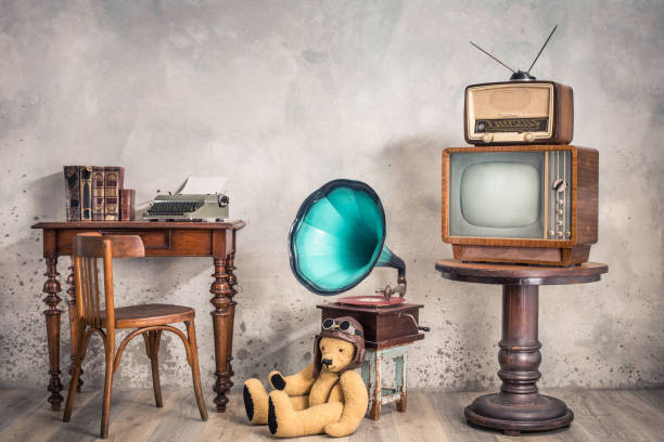 retro tv receiver, old broadcast radio from circa 50s on wooden table, outdated phonograph, teddy bear toy, workplace desk with typewriter, old books and chair. vintage style filtered photo - writing typewriter 1950s style retro revival imagens e fotografias de stock