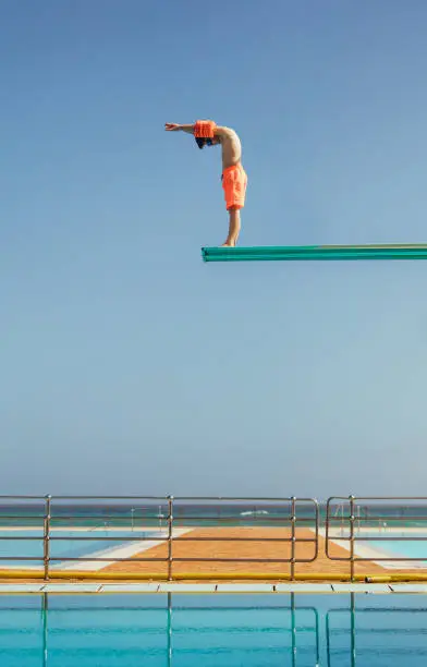 Boy stands on a diving platform about to dive into the swimming pool. Boy standing on high diving spring board preparing to dive.