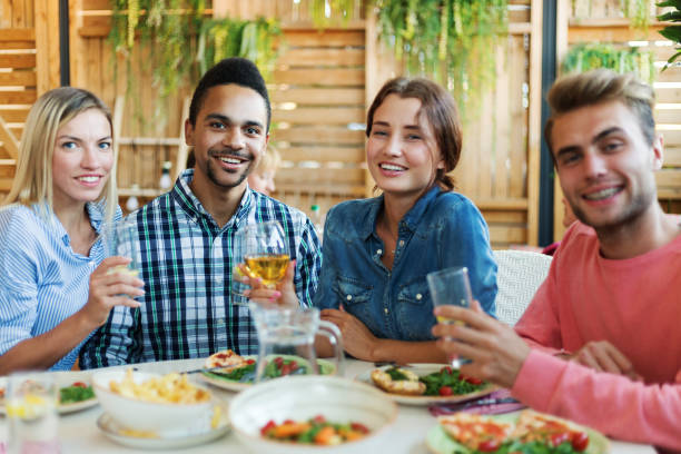 istock Two young couples posing with glasses of drinks at dining table in restaurant and smiling at camera 1140120434