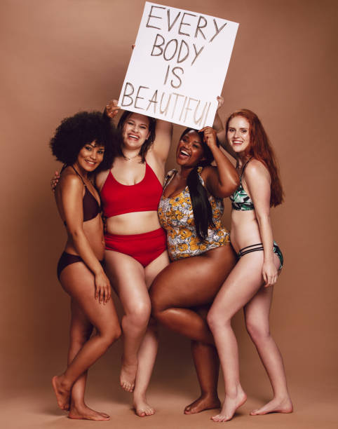 Diverse female group with every body is beautiful placard Excited group of women holding a every body is beautiful signboard over brown background. Multi-ethnic females of different figure and size looking excited together with a placard. body positive stock pictures, royalty-free photos & images