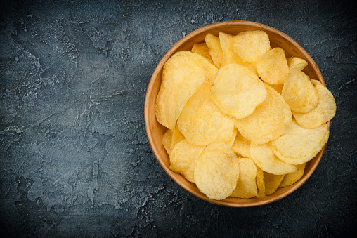 Crispy potato chips in bowl on dark rustic table. Overhead view with copy space.