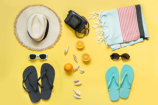 Beach accessories for two, straw beach sunhat,towel, sun glasses on yellow with space for text. Summer concept.