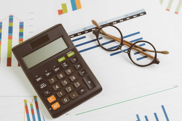 istock Black calculator, eyeglasses on monthly graph and chart on office table using as company profit and loss, financial and accounting activities 1140123852