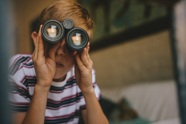 Small boy looking outside window using binoculars. Boy looking through binoculars from the living room.