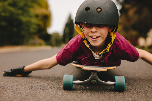 Small boy lying on his skateboard using his hands to guide while riding outdoors. Funny boy with helmet lying on skateboard.