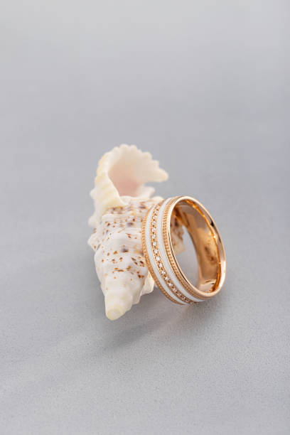 istock Gold ring with white enamel and diamonds on gray background with seashell 1140127088