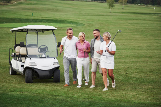 junge paare, die sich auf das spiel vorbereiten. eine gruppe lächelnder freunde kam auf einem golfwagen ins loch - retirement golfer happiness relaxation stock-fotos und bilder