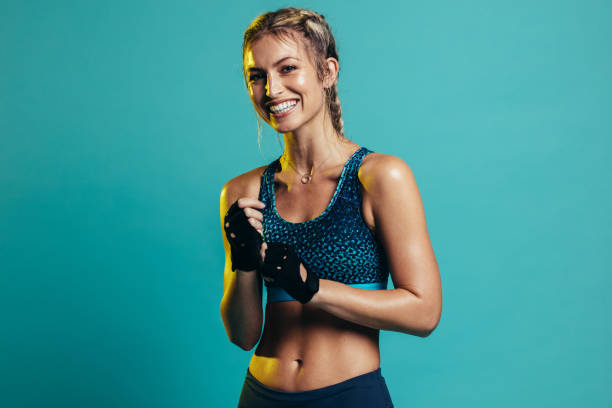 Smiling female fitness model Happy young woman in sports clothing smiling. Muscular fitness model on blue background looking at camera. sports bra stock pictures, royalty-free photos & images