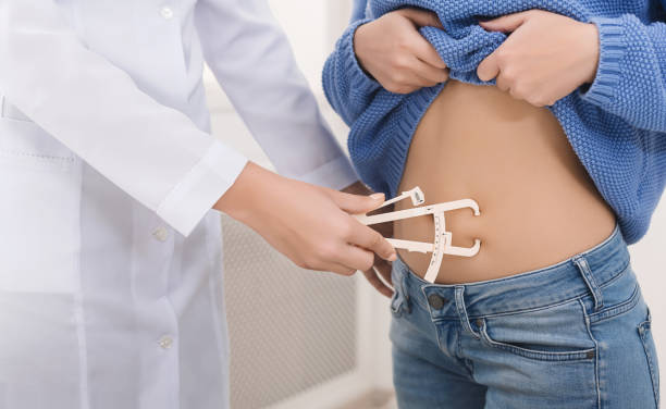 Doctor nutritionist measuring body fat to female patient BMI studying. Doctor nutritionist measuring fat layer of young woman with caliper in clinic, close up caliper photos stock pictures, royalty-free photos & images