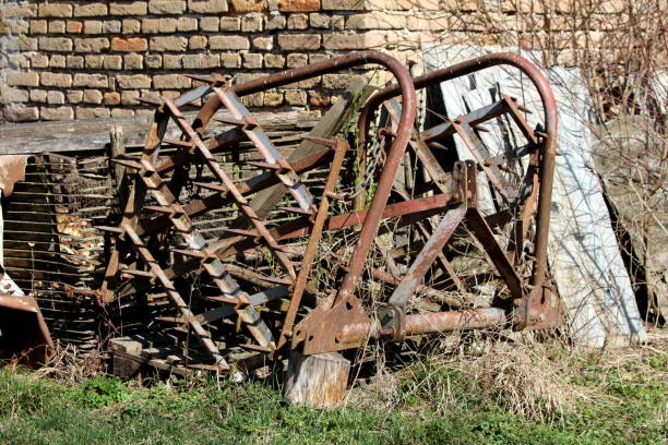 istock Rusted old vintage harrows left in backyard partially overgrown with dried grass surrounded with metal and construction material in front of red brick wall 1140134318