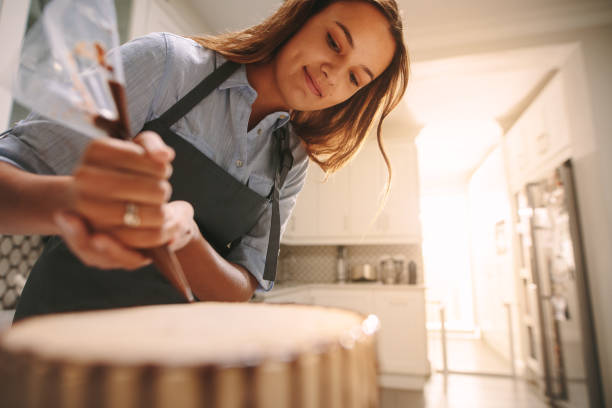 Pastry chef making a delicious cake Female pastry chef decorating a cake with chocolate in kitchen. Woman wearing an apron making a delicious cake at home. decorating a cake photos stock pictures, royalty-free photos & images