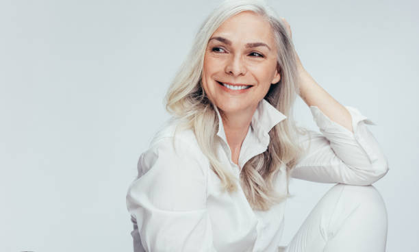 Beautiful senior woman looking at copy space Beautiful senior woman in white casuals looking away and smiling. Cheerful mature woman sitting on white background. middle aged woman fashion stock pictures, royalty-free photos & images