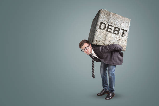 Businessman bending under a heavy stone with the word "DEBT" written on it stock photo