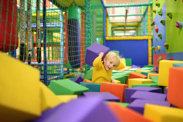 niedlicher kleiner junge spielt mit weichen würfeln im trockenen becken im spielzentrum. kind spielt auf indoor-spielplatz in schaumgummigrube im trampolin. - entertainment center fotos stock-fotos und bilder