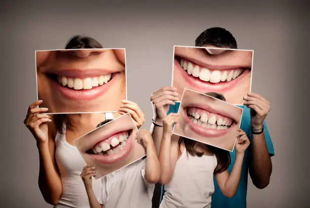 young family with children holding a picture of a mouth smiling on a gray background