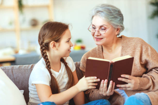 szczęśliwa babcia rodzinna czytana do książki wnuczka w domu - grandmother reading child grandson zdjęcia i obrazy z banku zdjęć