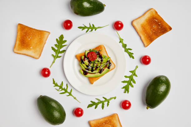 top view of toasts on plate with avocados, cherry tomatoes and arugulas leaves on grey background