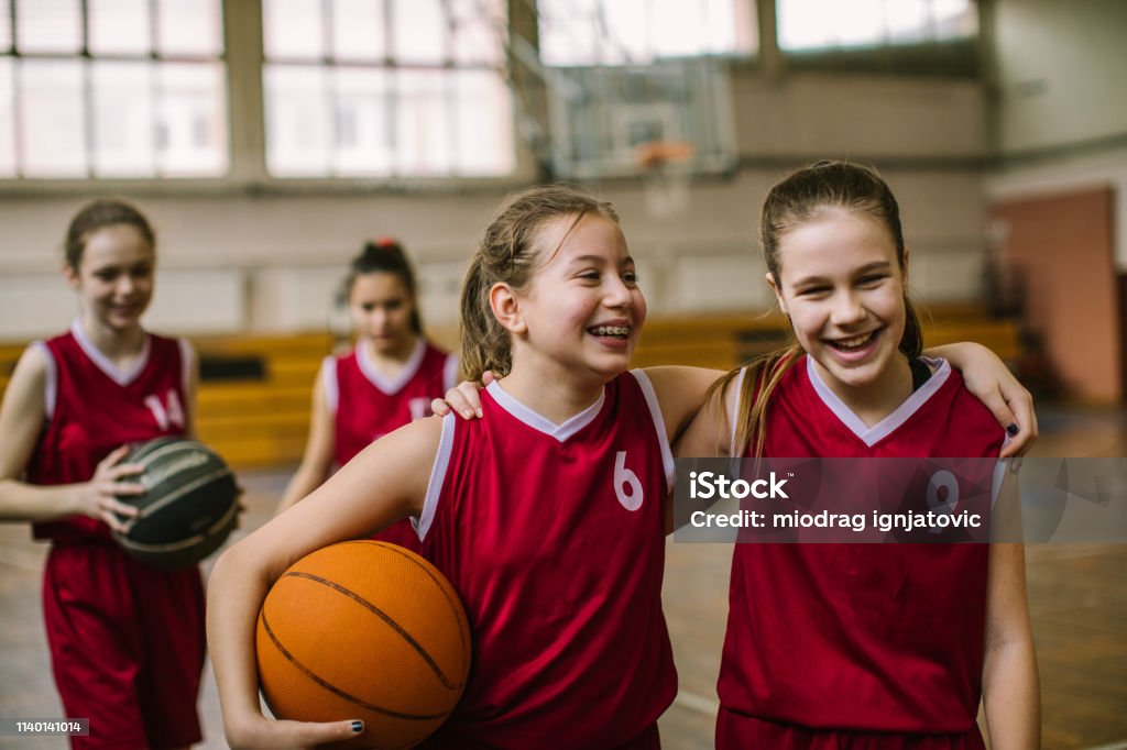 Friendship on basketball court Cute teenage girls, smiling and hugging after basketball match, happy after winning the game Child Stock Photo