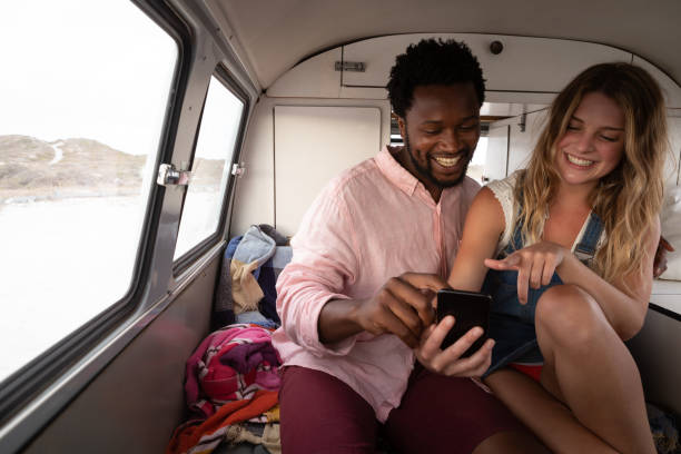 istock Couple laughing while they are using mobile phone in camper van at beach 1140142603