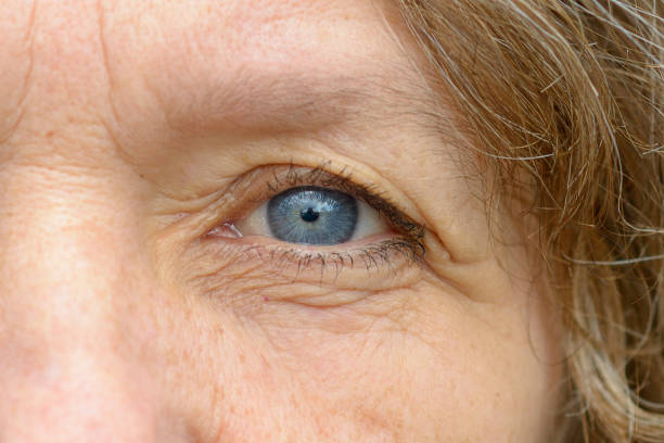 Close up of one pale blue eye of middle age woman with wrinkles. Full frame detailed portrait