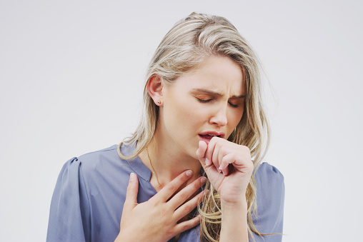 Studio shot of an attractive young woman coughing against a grey background