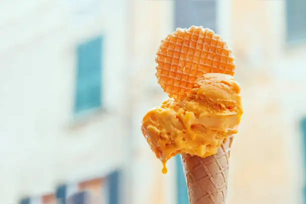 melting mango ice cream in brown waffle horn on sunny hot day against the backdrop of the ancient street in Vernazza, Liguria, Cinque Terre, Italy