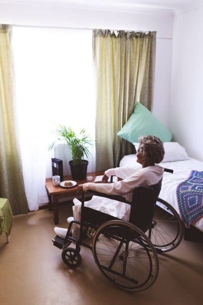 介護老人ホームで車椅子に座る思慮深い先輩女性 - healthcare and medicine home interior side view vertical ストックフォトと画像
